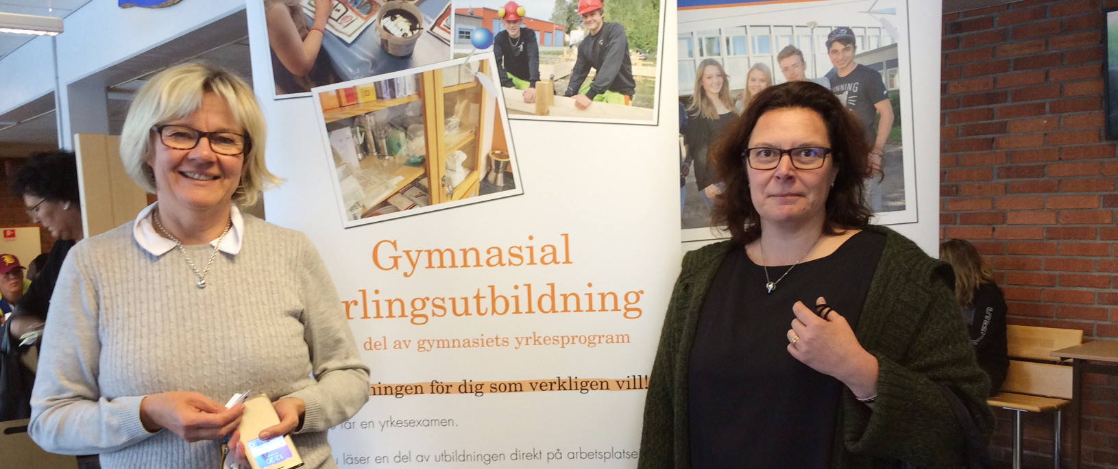 Två kvinnor står framför ett plakat som handlar om gymnasial lärlingsutbildning.