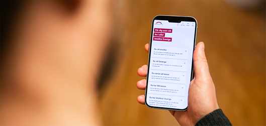 Person holding a mobile phone showing the new Swedish Migration Agency's website.