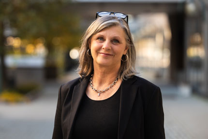 Portrait of Mari Mild, Director Human Resources Department. he stands outside in a dark shirt and a dark jacket.