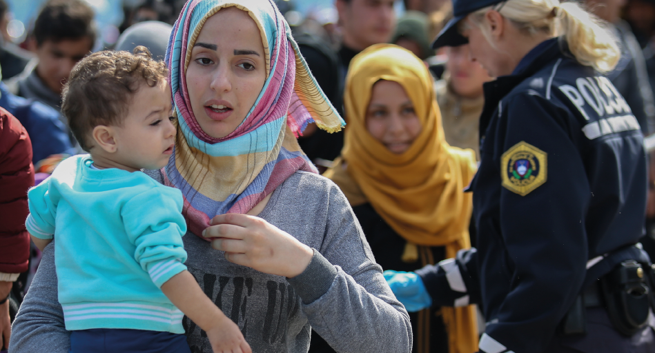 Kvinnor med barn i famnen går i en folkmassa under flykt. De bär färgglada hijabs.