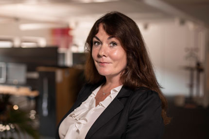 Portrait of Anna Lindblad, Deputy Head of Office of the Director-General. She stands indoors in a light shirt and a dark jacket.