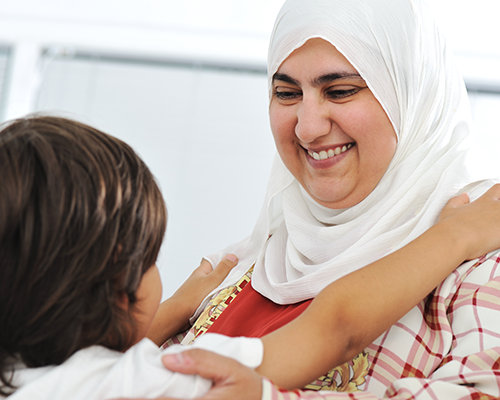 Leende kvinna i vit hijab som kramar ett barn.
